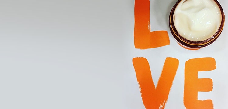 Overhead shot of LOVE characters written in orange paint while O is covered with GinZing Gel moisturizer jar with cap off 